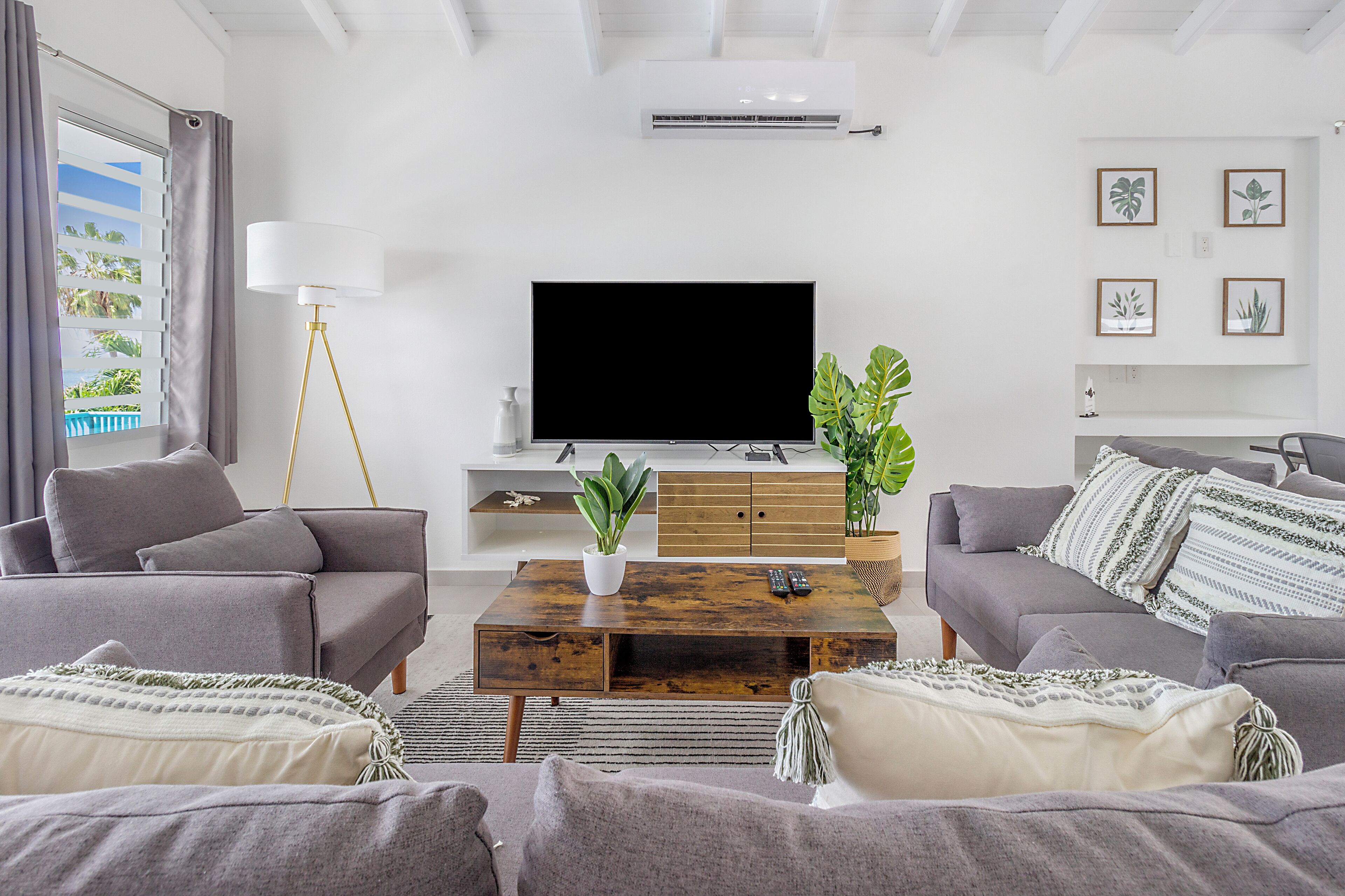 Ein modernes Wohnzimmer mit einem Flachbildfernseher, grauen Sofas, einem Holztisch und einem Topfpflanze.