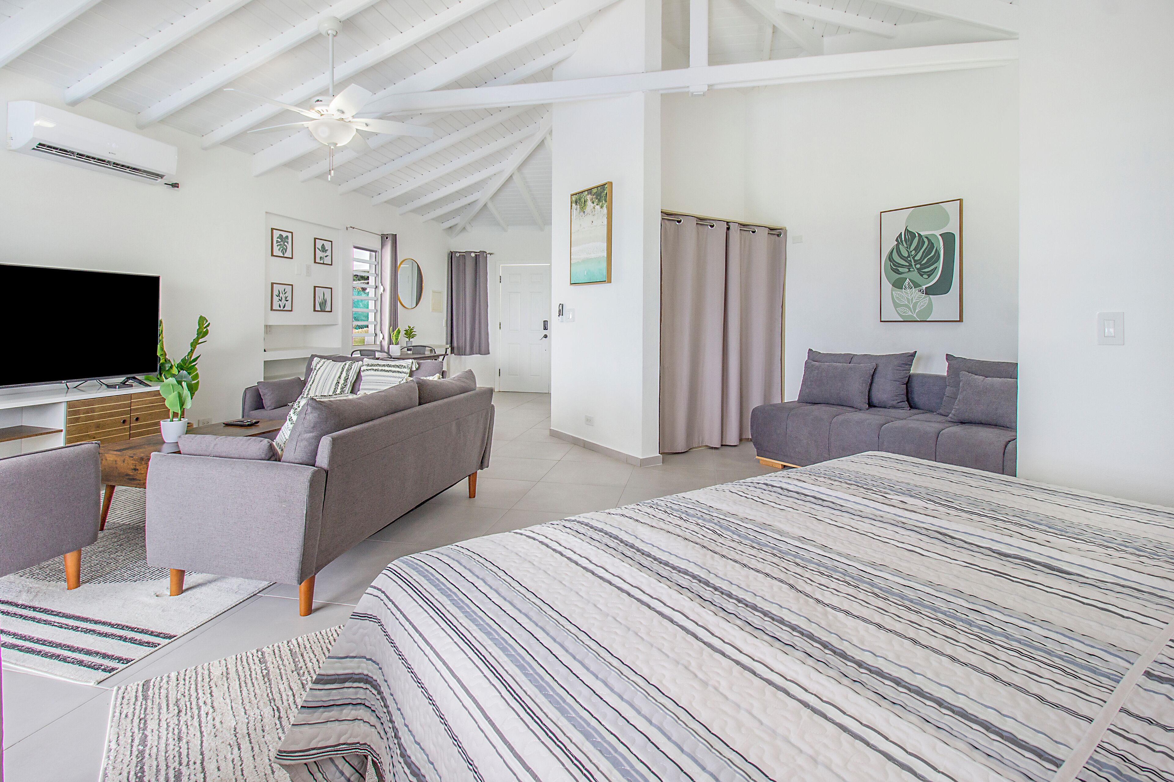 A spacious living area with a large bed, two sofas, a flat-screen TV, and a ceiling fan.