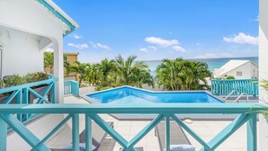 A pool area with a view of the ocean, surrounded by palm trees and a turquoise railing.