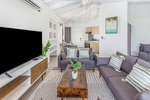 Een moderne woonkamer met een flatscreen televisie, een salontafel met een plant en een grijze bank met decoratieve kussens.