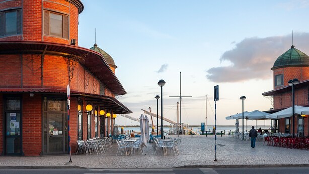 A waterfront building with a brick facade, multiple dining areas with outdoor seating, and a statue in the center. - Casa da Guida Olhão Portugal (Olhão)