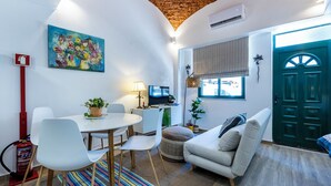 A cozy living room with a round dining table, white chairs, a sofa, a TV, and a colorful rug. - Casa da Guida Olhão Portugal (Olhão)