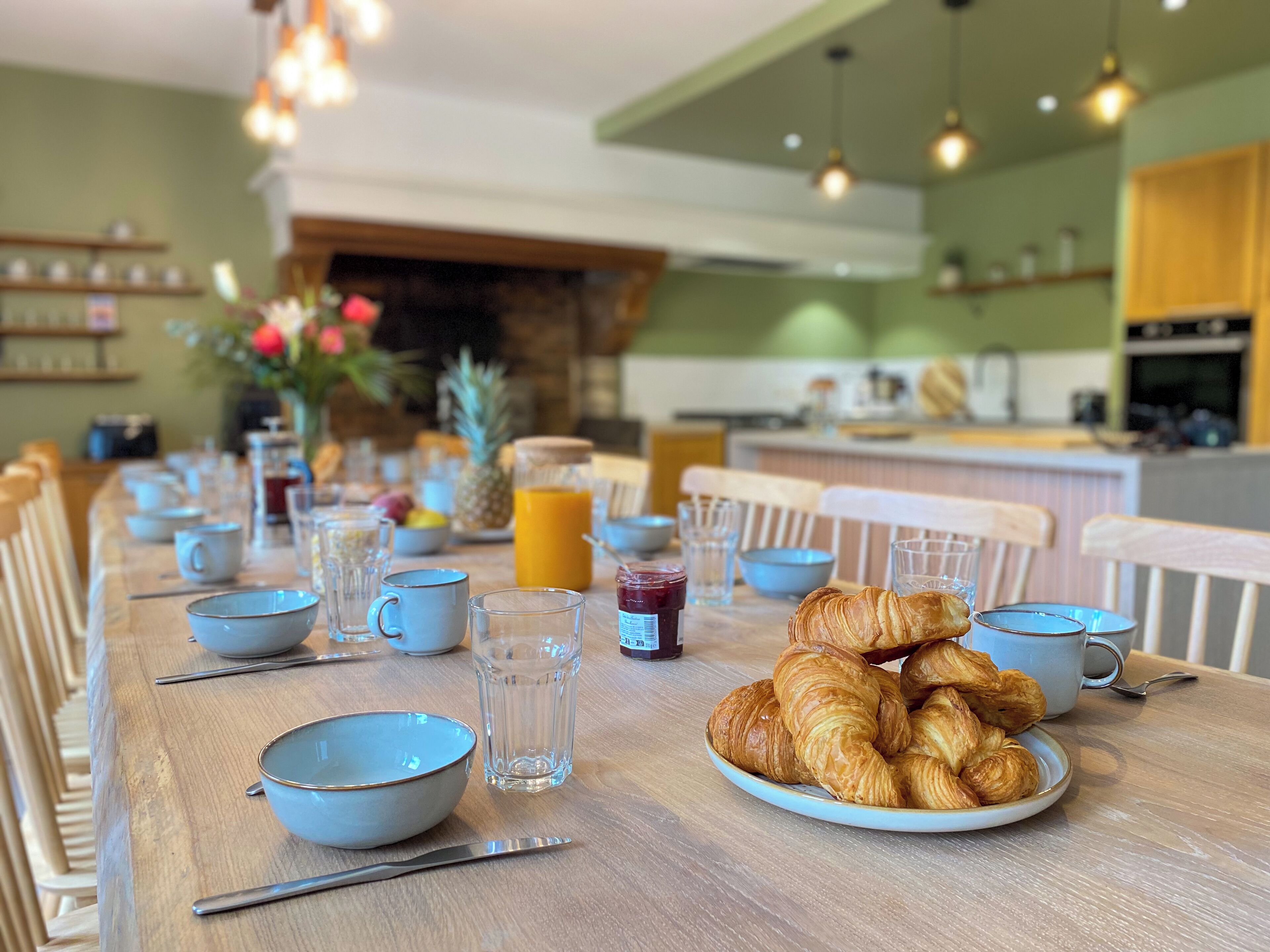 A breakfast table set with bowls, cups, a plate of croissants, and a glass of orange juice.