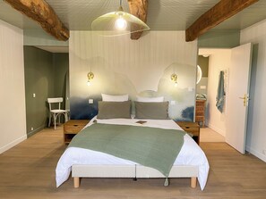 Une chambre à coucher avec un lit, une tête de lit en bois, deux tables de chevet, un plaid vert et un luminaire suspendu.