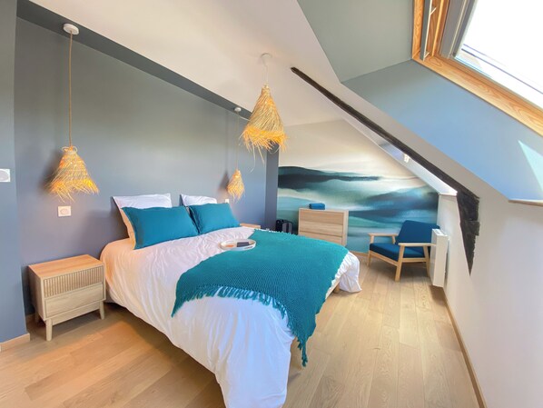 Une chambre moderne avec un grand lit, deux tables de chevet, une chaise et un plafond doté d’une lucarne.