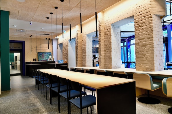 A modern restaurant with long communal tables, black chairs, and stone pillars.
