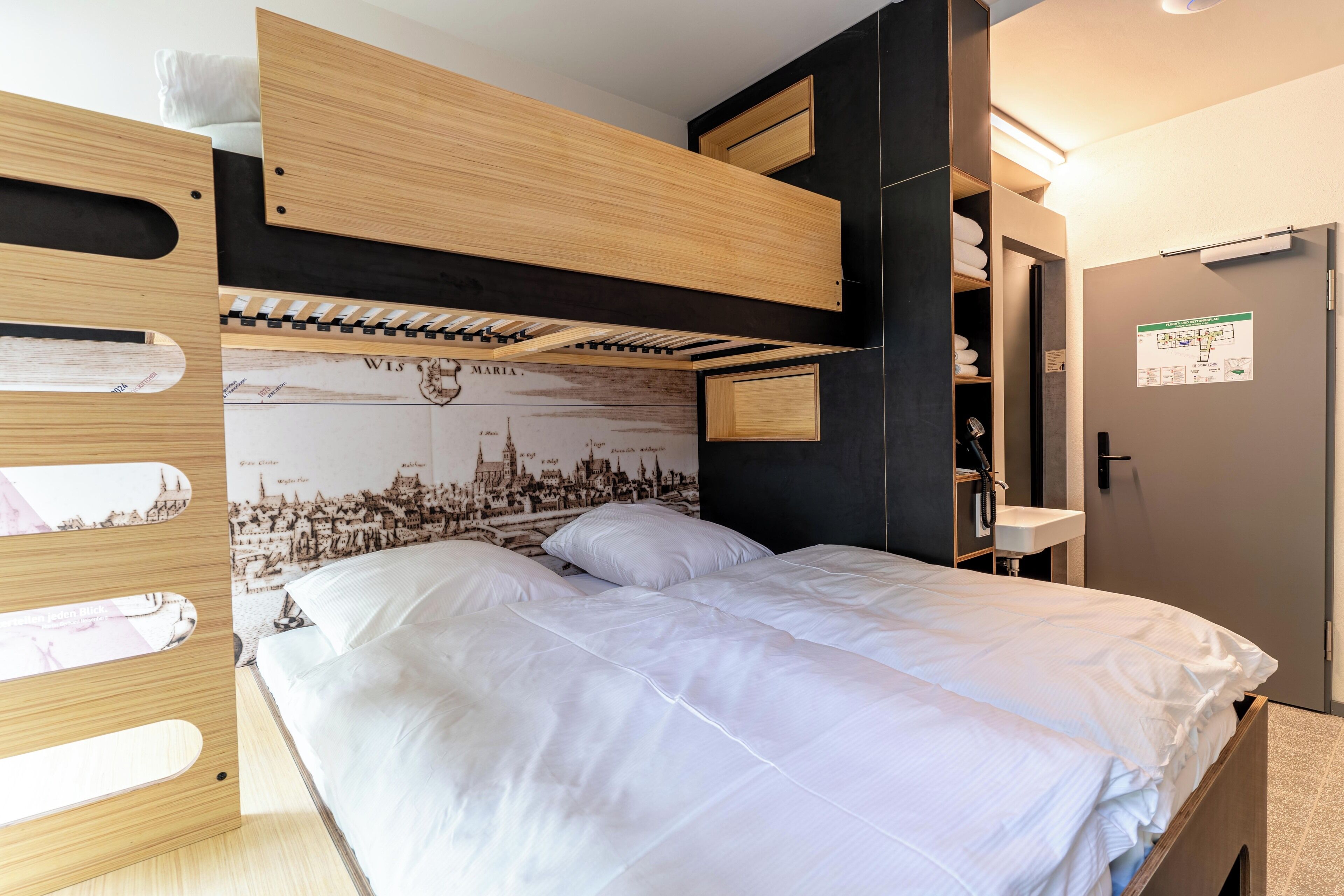 A bunk bed with a cityscape mural, a wooden headboard, and a built-in shelf with towels.