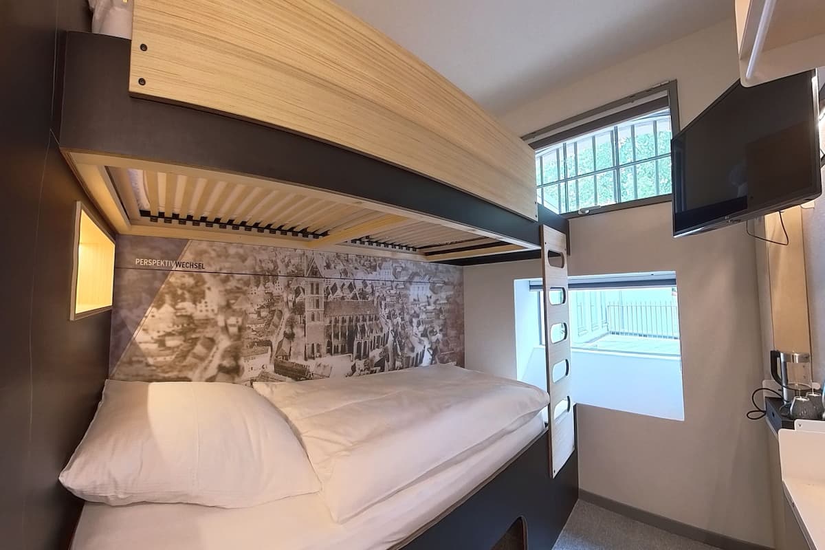 A bunk bed with a cityscape mural on the headboard, a window with a view, and a mounted TV.