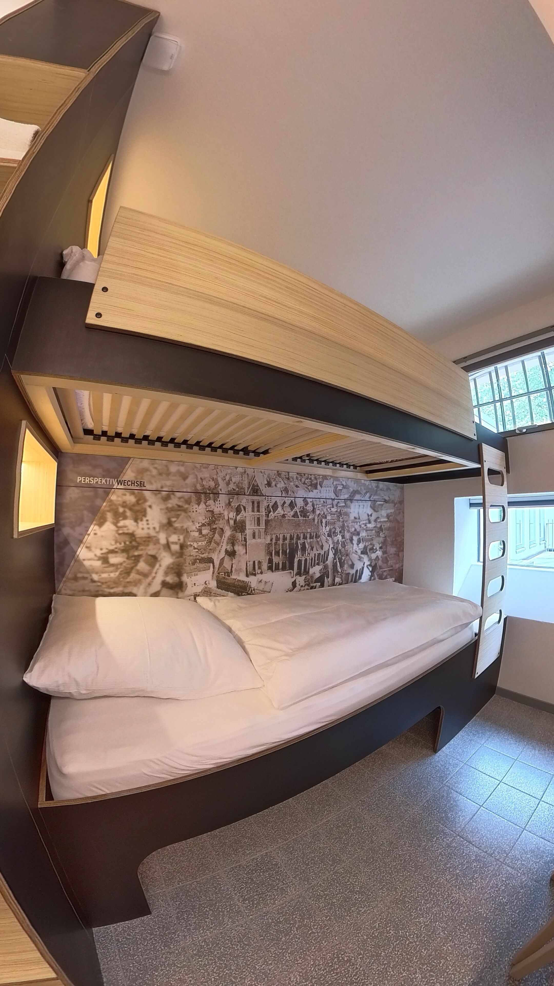 Un dormitorio moderno con una litera, un mural grande en la pared y una ventana que proporciona luz natural.