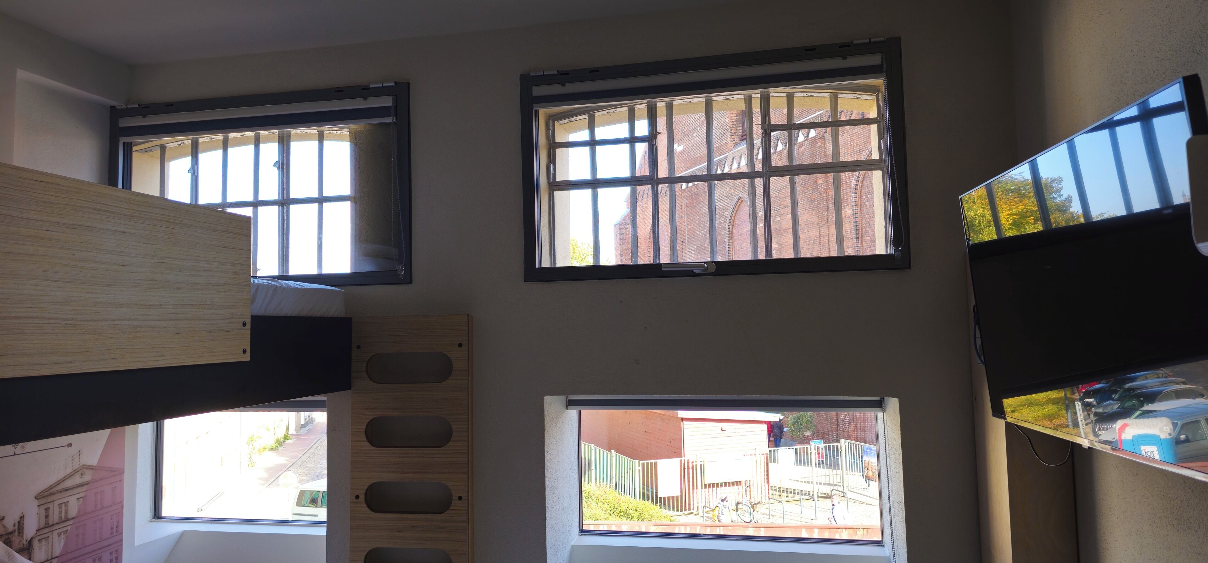 Una habitación con varias ventanas, una litera y vista a un edificio y una calle.