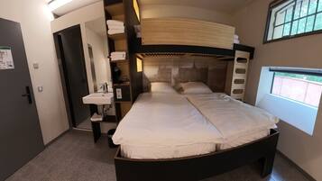 A bedroom with a bunk bed, a bedside table, a sink, and a window with a view.