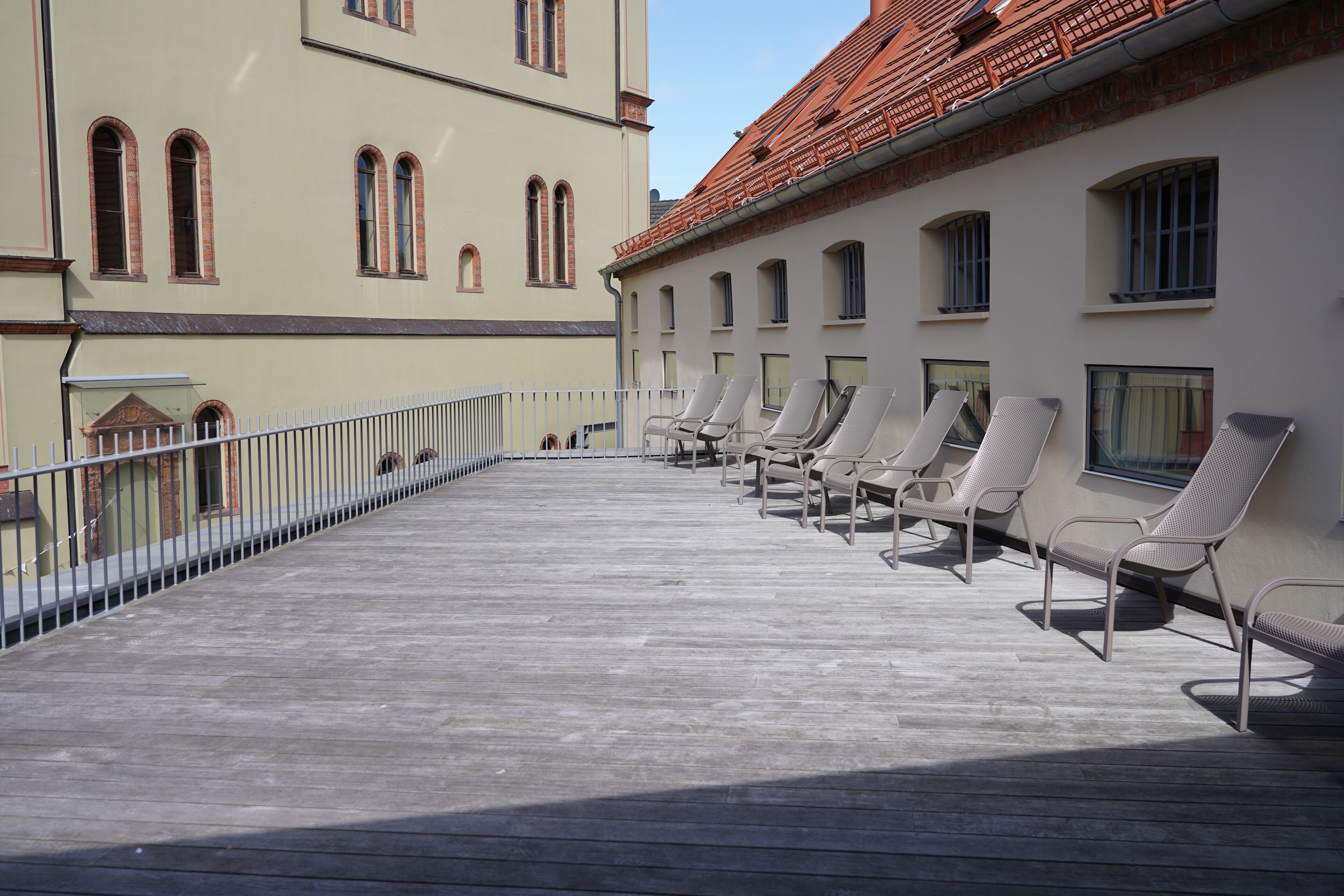 Ein Balkon mit Liegestühlen, einem Geländer und einem Gebäude mit Rundbogenfenstern und einem Ziegeldach.