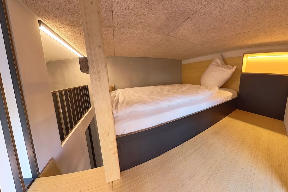 A compact, modern room with a single bed, built-in storage, and a sloped ceiling.