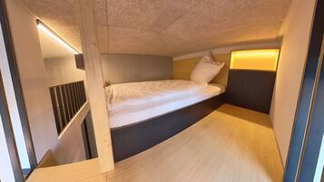Habitación compacta y moderna con cama individual, almacenaje integrado y techo inclinado.