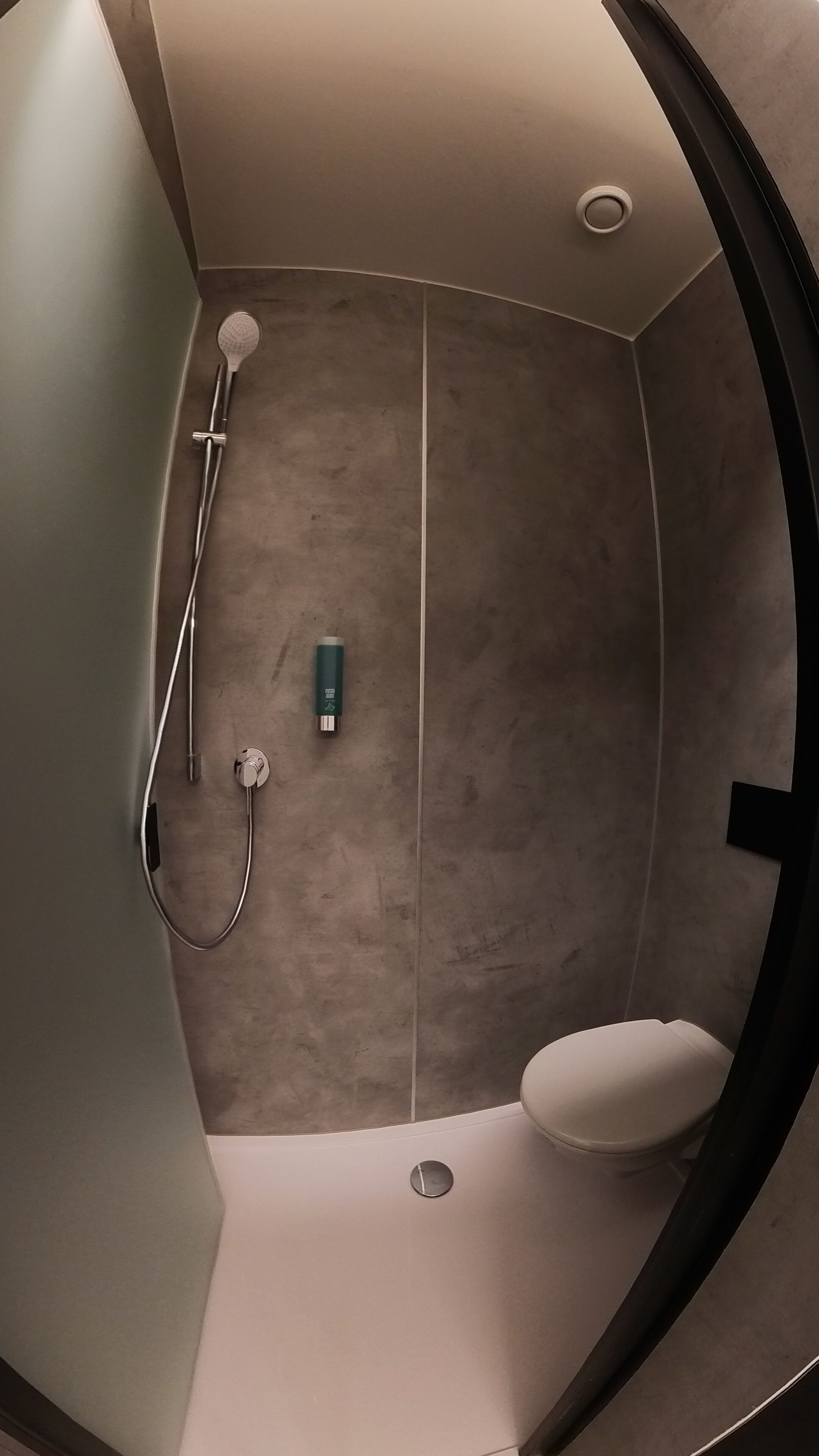 Une salle de bain avec une douche, des toilettes et une bouteille de shampoing.