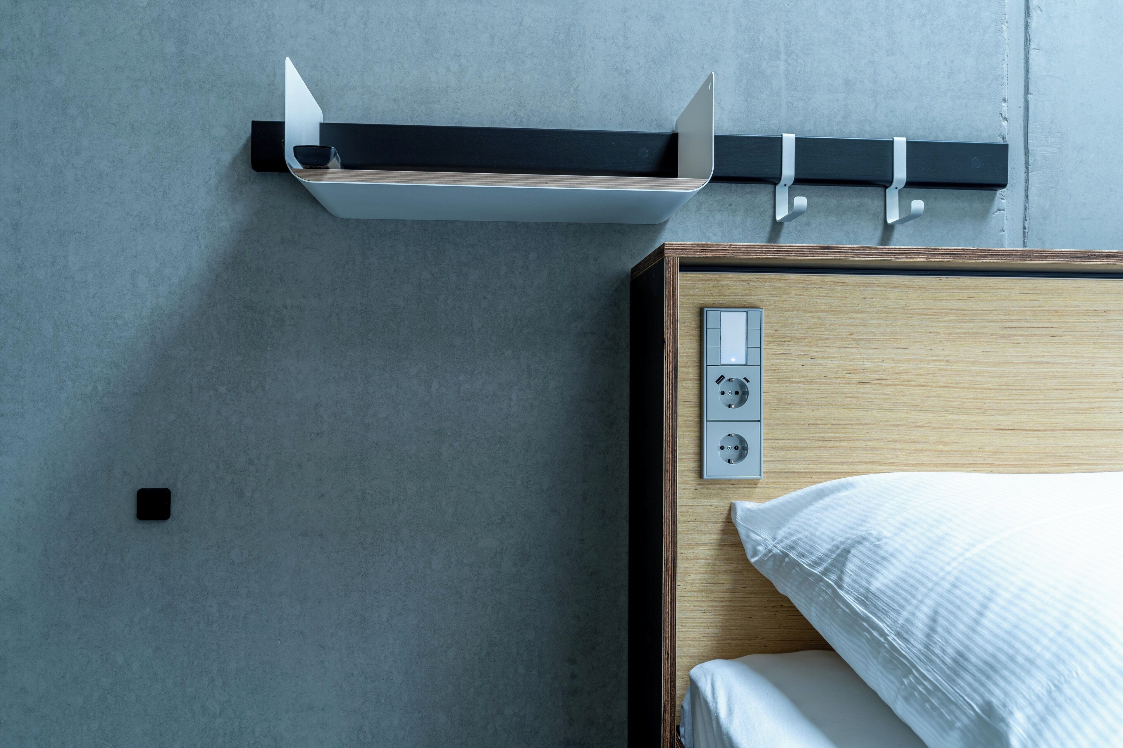 A modern hotel room with a wooden bed, a built-in shelf, and a wall-mounted power outlet.