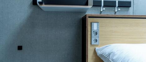 A modern hotel room with a wooden bed, a built-in shelf, and a wall-mounted power outlet.