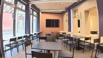 Un salón de conferencias con mesas y sillas, ventanas amplias y un televisor de pantalla plana en la pared.