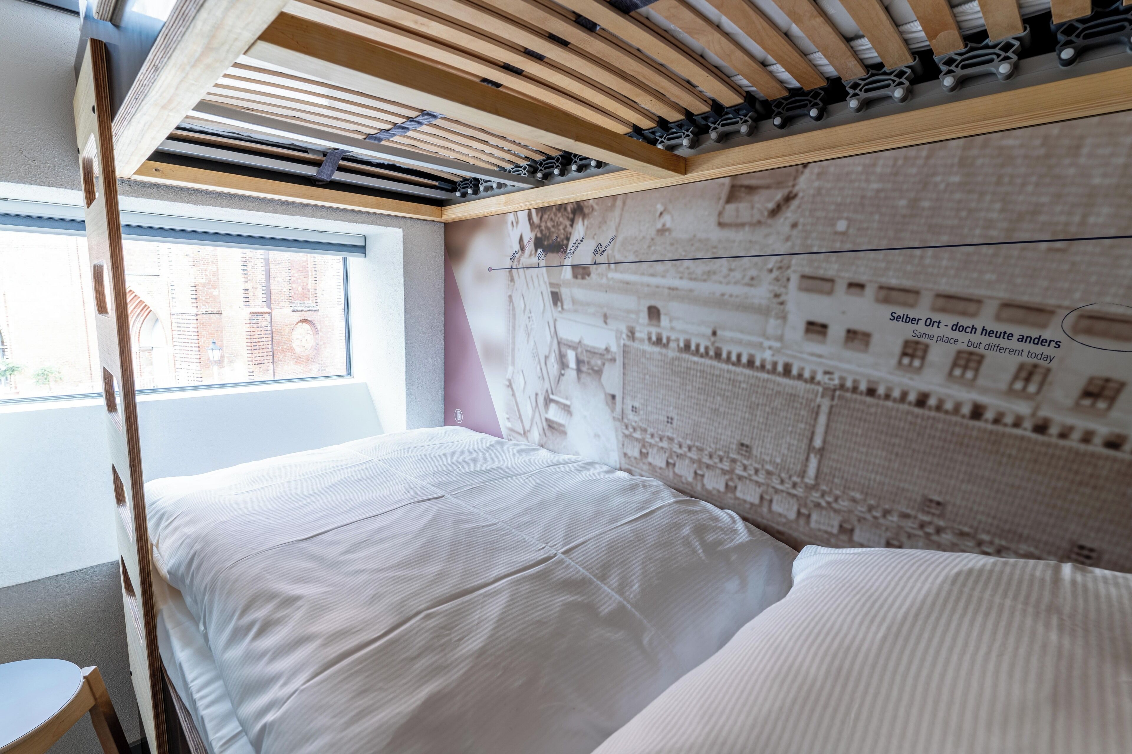 A modern bedroom with a bunk bed, a large window, and a cityscape mural on the wall.