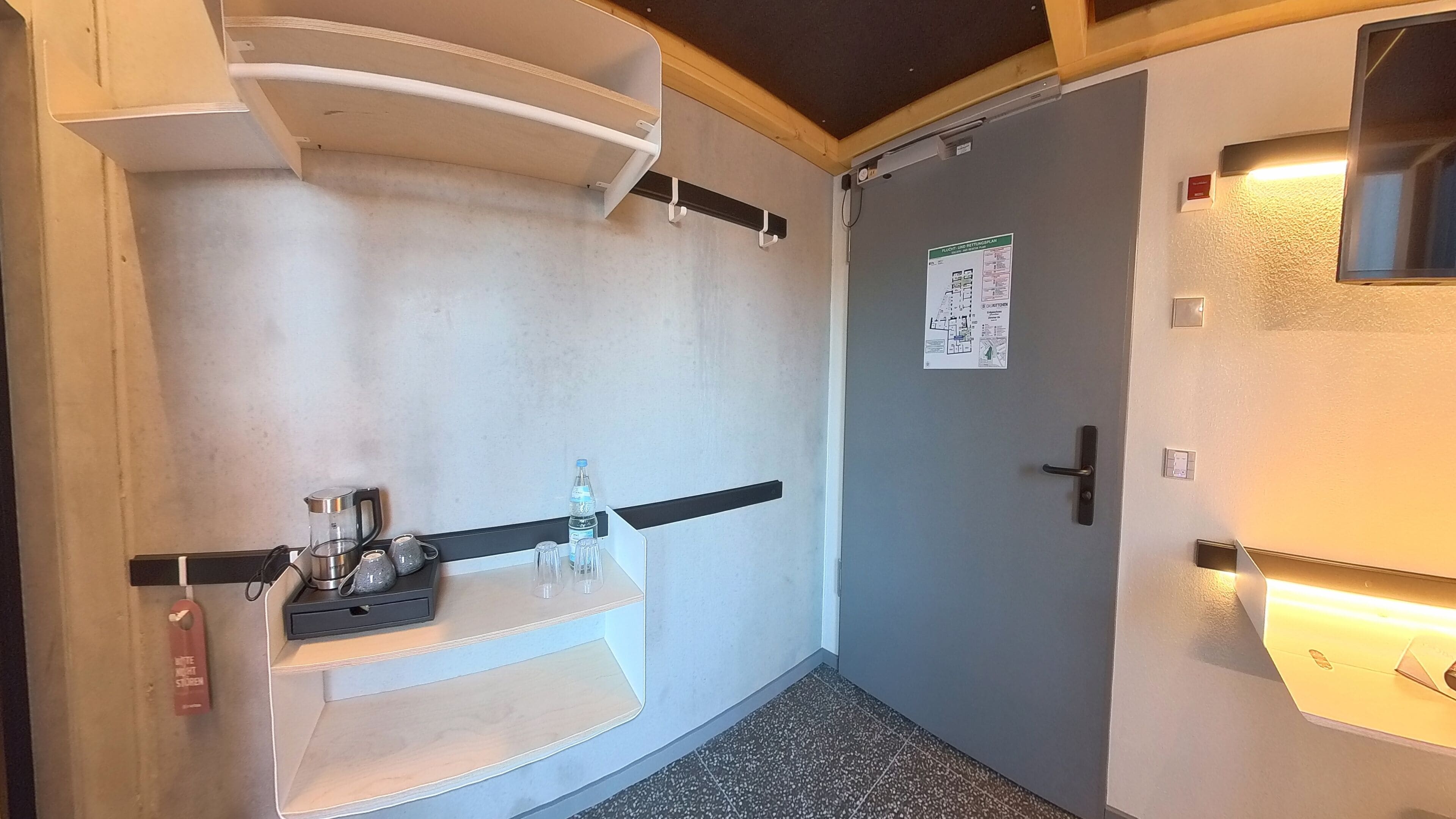 Un couloir étroit avec un petit coin cuisine, une porte ornée d’une carte et un téléviseur fixé au mur.