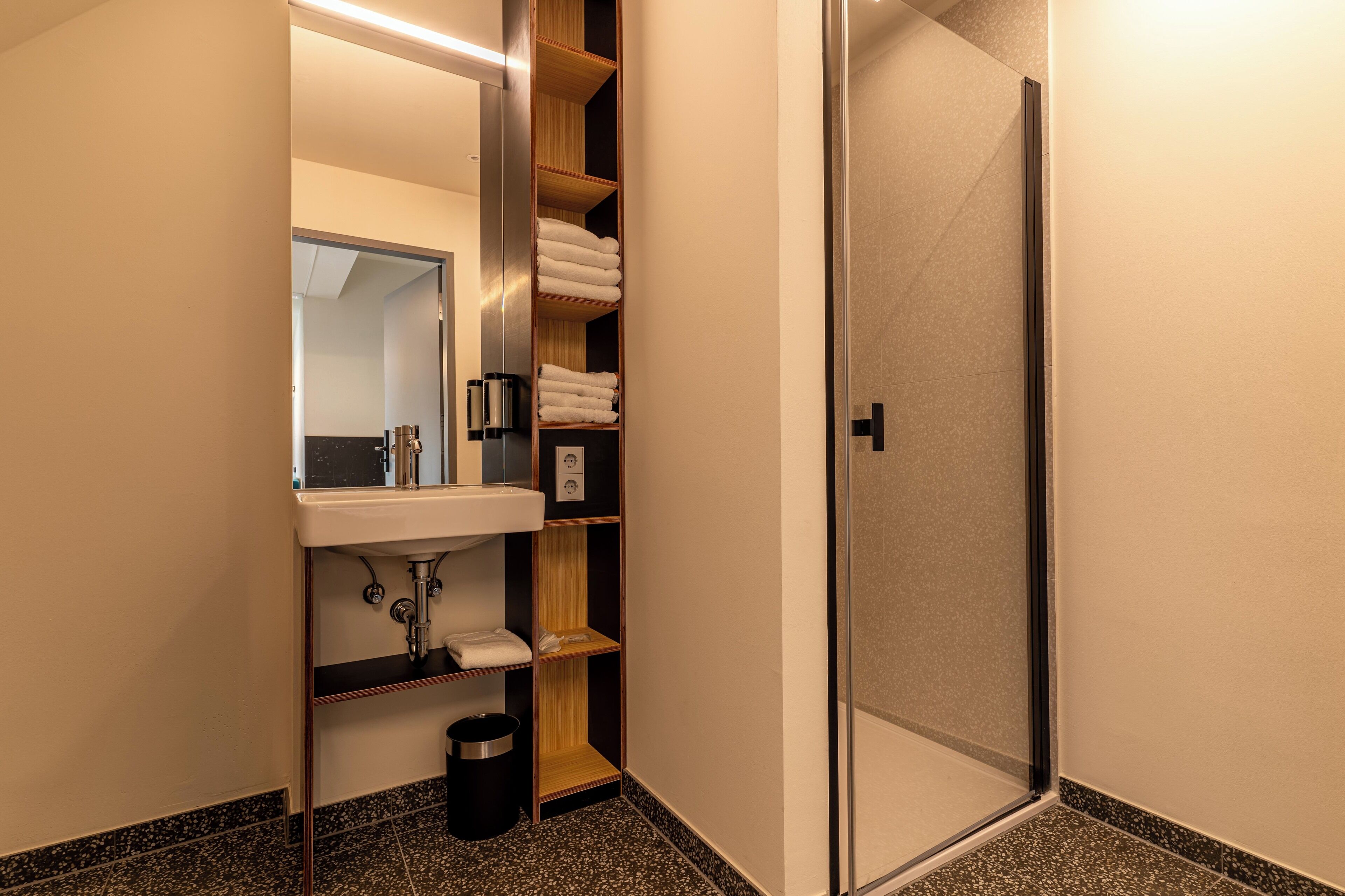 Ein modernes Badezimmer mit Waschbecken, Spiegel, Handtuchhalter und einer Duschkabine aus Glas.