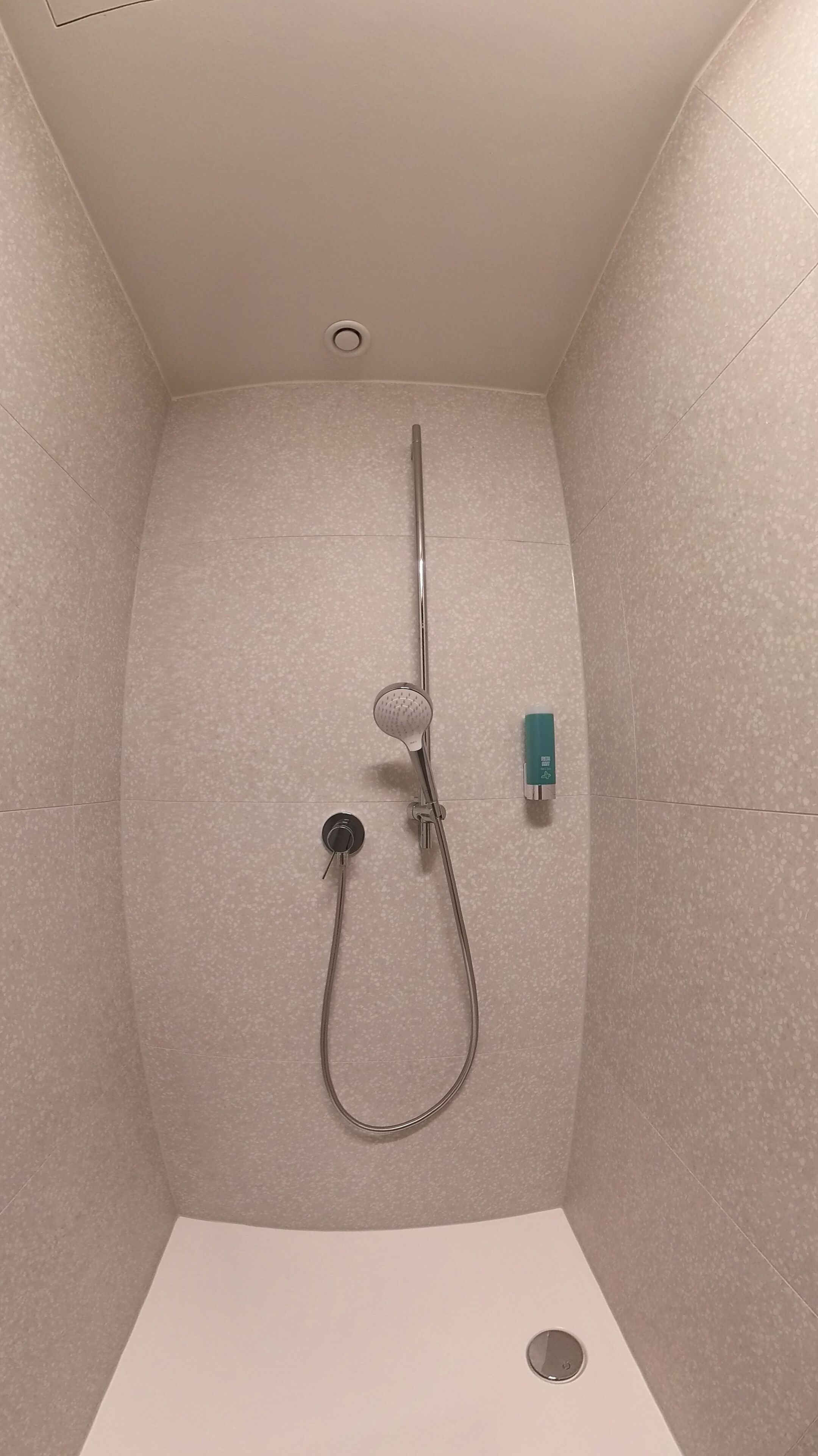 Una ducha con cabezal de ducha manual, grifo empotrado y dispensador de jabón.