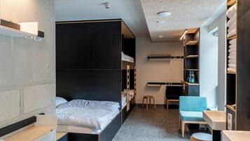 Habitació d'hotel petita amb literes, escriptori, cadira i petit tamboret.