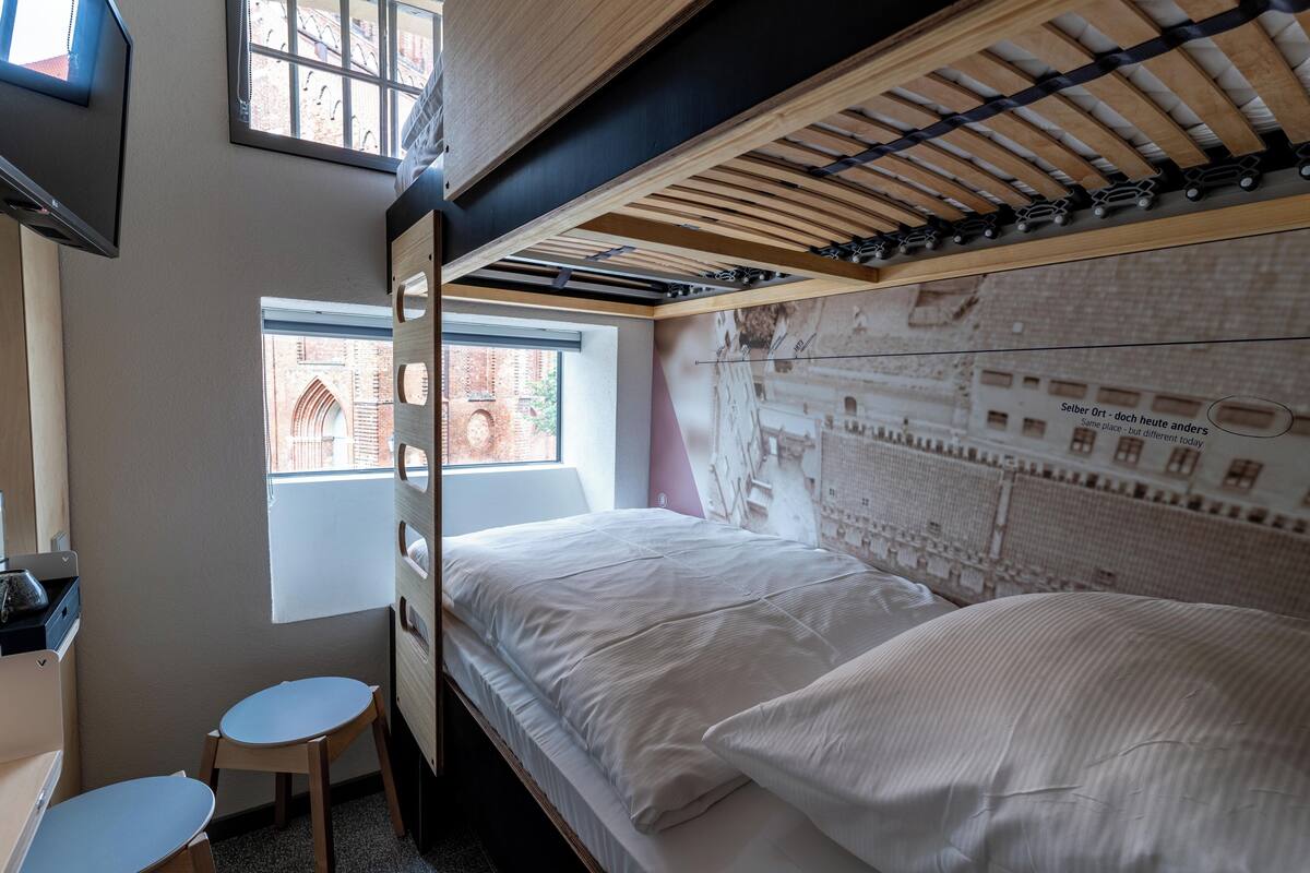 A bunk bed room with a window, a desk, and a chair.