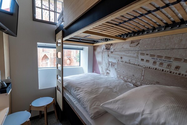 A bunk bed room with a window, a desk, and a chair. - Das Kittchen (Wismar)
