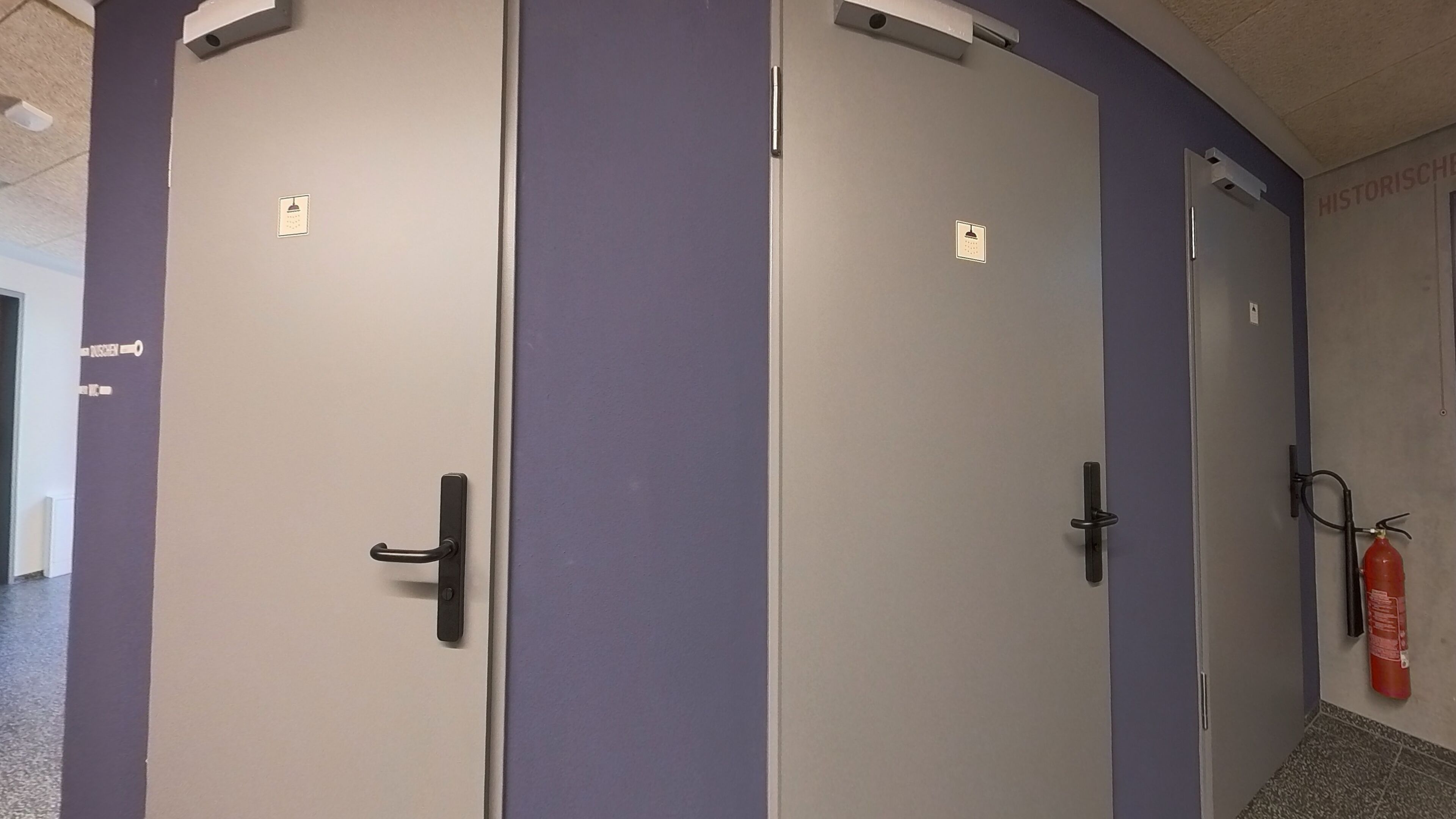 Ein Flur mit zwei Türen, eine mit Griff und eine mit Schlüsselloch, sowie ein an der Wand befestigter Feuerlöscher.