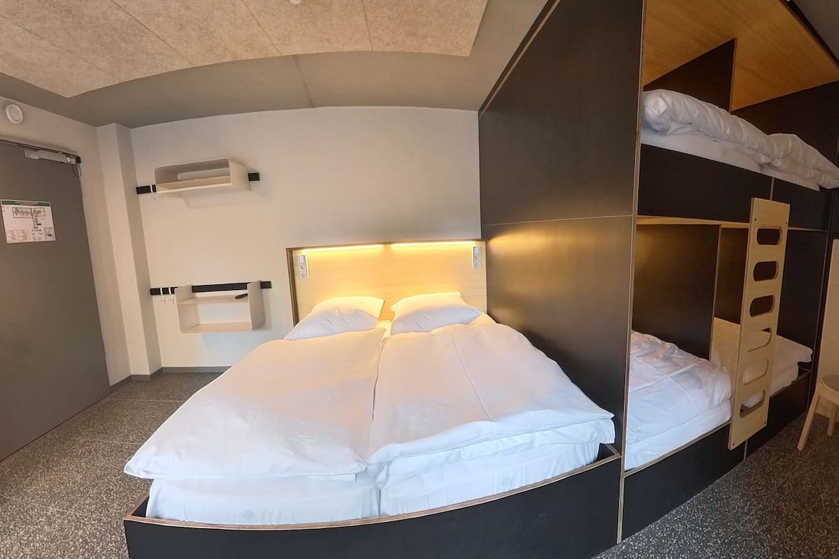 A bunk bed room with a desk and chair, a headboard with a light, and a small shelf.