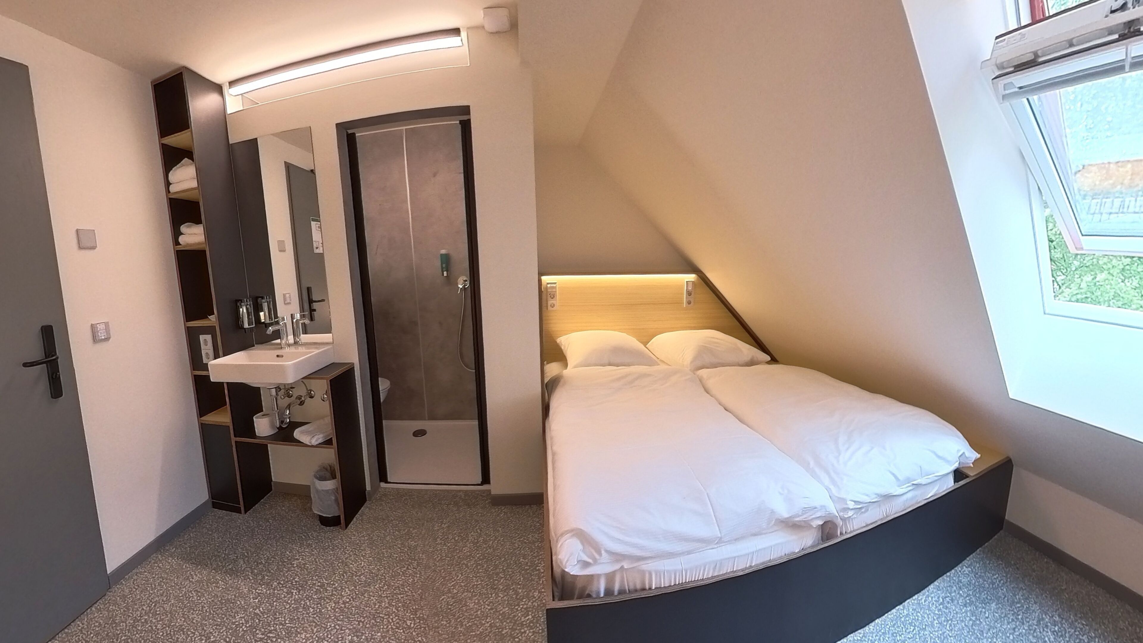 A compact bedroom with a bed, a built-in wardrobe, a sink, and a window.