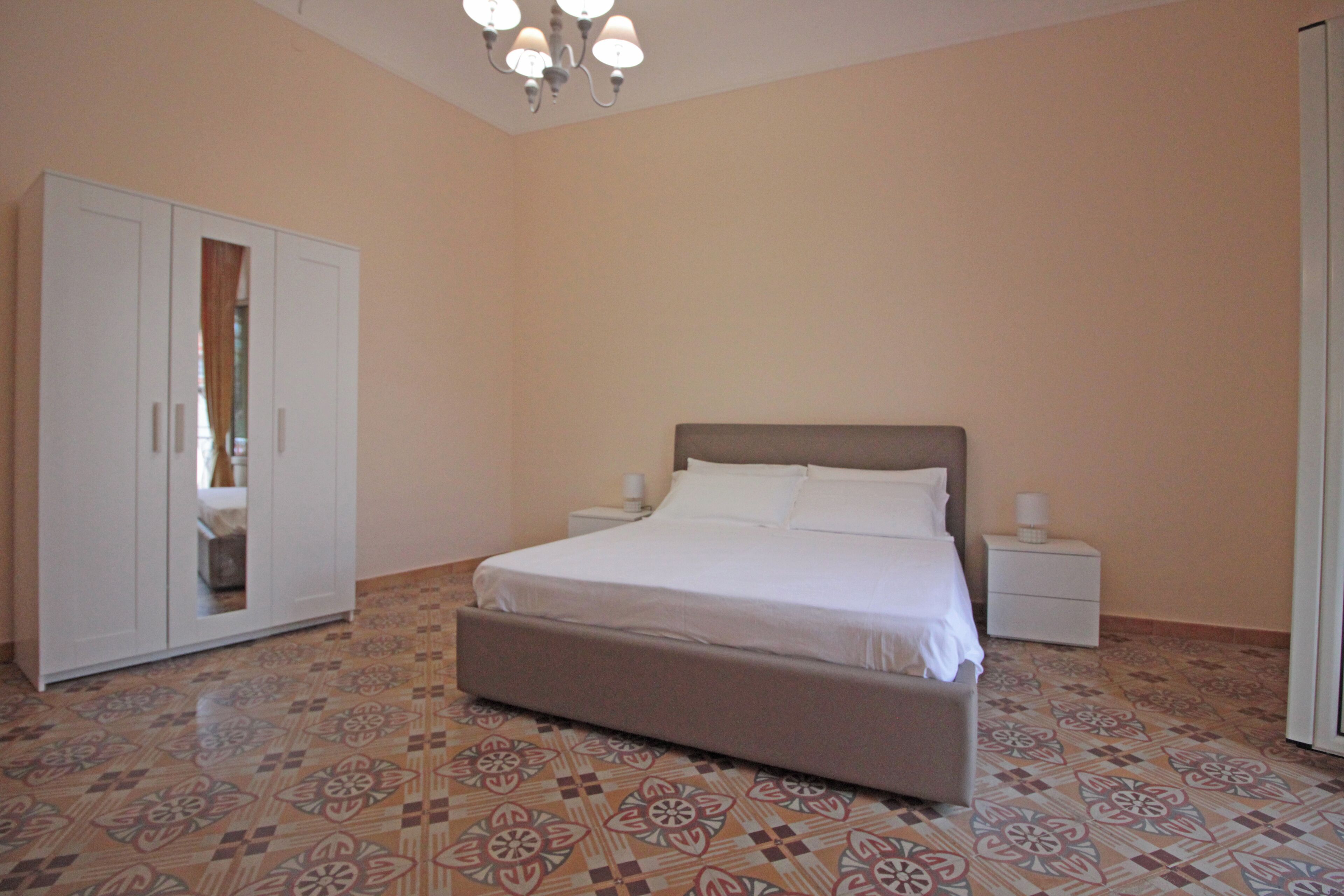 A bedroom with a bed, nightstands, a wardrobe, and patterned flooring.