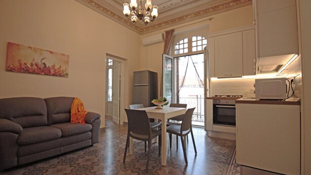 A living room with a sofa, dining table, chairs, and a kitchen area with a refrigerator, microwave, and oven. - Moro Central Apartment by Wonderful Italy (Cefalù)