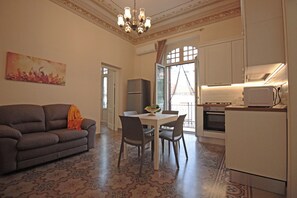 A living room with a sofa, dining table, chairs, and a kitchen area with a refrigerator, microwave, and oven. - Moro Central Apartment by Wonderful Italy (Cefalù)