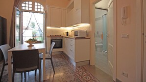 A compact kitchen with white cabinets, a microwave, and a dining area with a table and chairs. - Moro Central Apartment by Wonderful Italy (Cefalù)