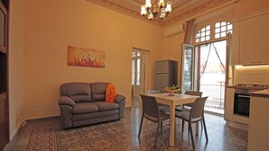 A living room with a sofa, dining table, chairs, and a chandelier. - Moro Central Apartment by Wonderful Italy (Cefalù)