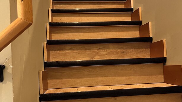 Un escalier en bois avec des contremarches noires et une main courante en bois.