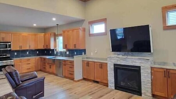A spacious kitchen with wooden cabinets, a large island, a fireplace, and a flat-screen TV mounted above it. - Fieldstone Manor Estate (Frankfort)