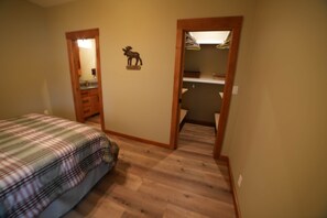 Un dormitorio con colcha a cuadros, una puerta de madera que da a un armario y un pequeño cartel de bienvenida en la pared.