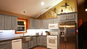 A kitchen with grey cabinets, a stainless steel refrigerator, a microwave, and a stove. - Elberta Bluffs Cottage (Elberta)