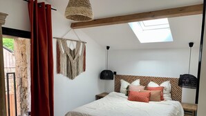 A bedroom with a large bed, a skylight, a macrame wall hanging, and a red curtain. - Charming Cottage 4* Spa & Activities - Luxury, Comfort & Nature near Futuroscope (Celle-Lévescault)
