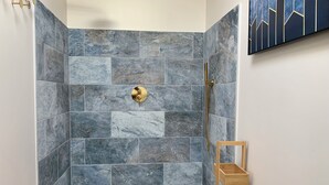 A shower area with a tiled wall, a gold shower head, and a wooden shelf. - Charming Cottage 4* Spa & Activities - Luxury, Comfort & Nature near Futuroscope (Celle-Lévescault)