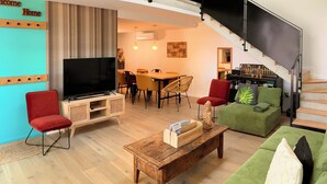A spacious living area with a TV, red and green sofas, a wooden coffee table, and a staircase leading to an upper level. - Charming Cottage 4* Spa & Activities - Luxury, Comfort & Nature near Futuroscope (Celle-Lévescault)