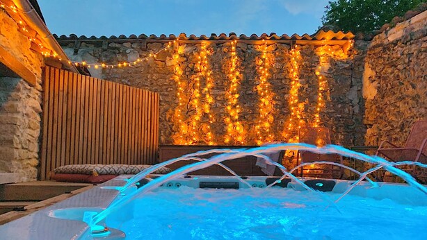 A hot tub with a stone wall and string lights in the background. - Charming Cottage 4* Spa & Activities - Luxury, Comfort & Nature near Futuroscope (Celle-Lévescault)
