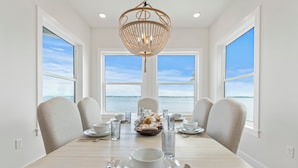 A dining room with a view of the sea, a chandelier, and a table set for four. - Dolphin Cove-Luxury Sound front retreat w/private pier.  6 bed/6.5 bath sleeps 1 (Navarre)