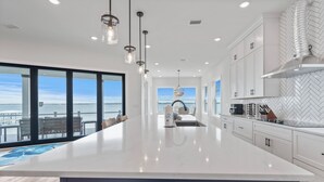 A modern kitchen with a large island, white cabinetry, and a view of the ocean. - Dolphin Cove-Luxury Sound front retreat w/private pier.  6 bed/6.5 bath sleeps 1 (Navarre)