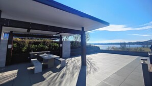 An outdoor patio with a covered seating area, a view of a body of water, and a distant landscape. - Lakeside apartment, walking distance to foreshore (Kingston)