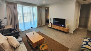 A modern living room with a flat-screen TV, a wooden coffee table, a sofa, and a guitar. - Lakeside apartment, walking distance to foreshore (Kingston)