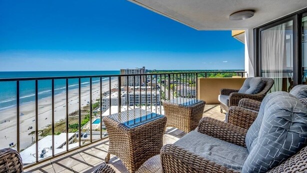 Een balkon met rieten meubilair, met uitzicht op een strand en de skyline van een stad.